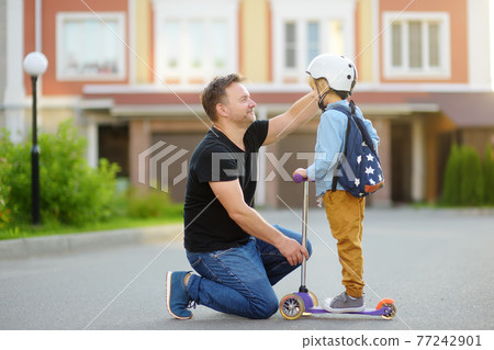 Little boy with scooter says goodbye and hugging to his father before going to school. Education for children. First day of school. Little boy with scooter says goodbye and hugging to his father before going to school. Education for children. First day of school. 77242901