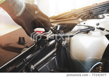 Mechanic hand is opening the radiator cap to check the coolant level of the car radiator 77242977