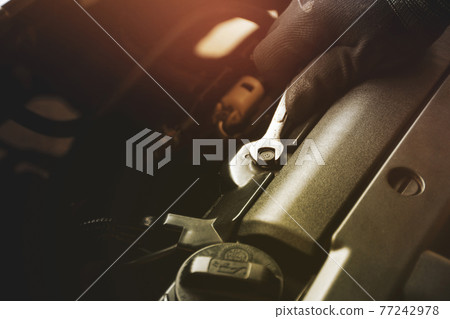 Mechanic hand is unscrewing the metal nut with a combination wrench 77242978