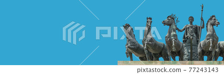 Banner with statue of Goddess Victoria with horses at the top of Triumphal Arch called Arch of Peace in Milan historical downtown, Sempione Park, Italy, at blue sky background with copy space 77243143