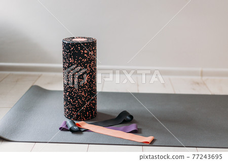 Black gymnastic roller lie with fitness rubber bands on the floor of a gym. Indoor and outdoor workout. Sport and healthy active lifestyle concept. Black gymnastic roller lie with fitness rubber bands on the floor of a gym. Indoor and outdoor workout. Sport and healthy active lifestyle concept. 77243695