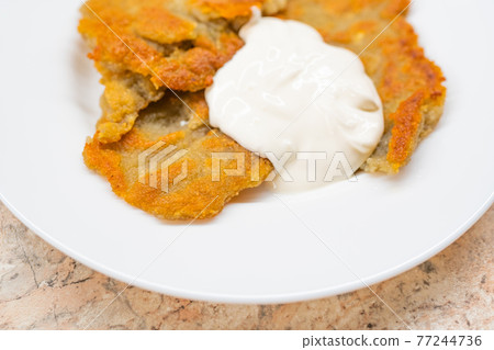 Potato pancakes with sour cream on ceramic white plate Potato pancakes with sour cream on ceramic white plate 77244736
