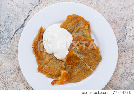 Potato pancakes with sour cream on ceramic white plate Potato pancakes with sour cream on ceramic white plate 77244738