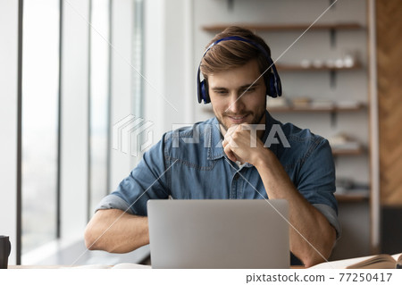 Smiling male in earphones study online on laptop Smiling male in earphones study online on laptop 77250417