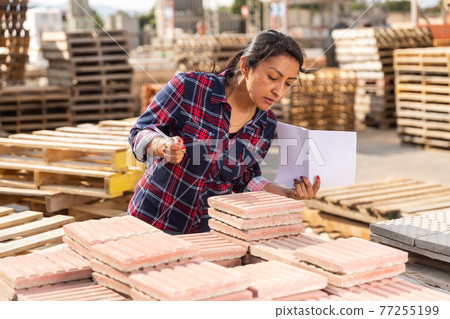 Female worker checking quantity of paving slabs in warehouse 77255199