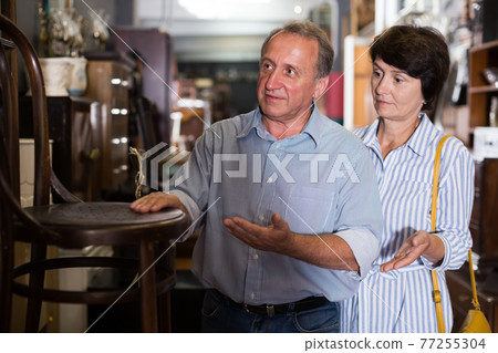 Adult woman with husband are buying antique armchair 77255304