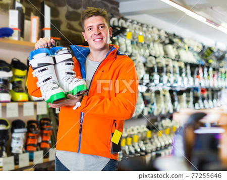 Adult man in jacket and helmet is demonstrating his choice of boots for skiing. Adult man in jacket and helmet is demonstrating his choice of boots for skiing. 77255646