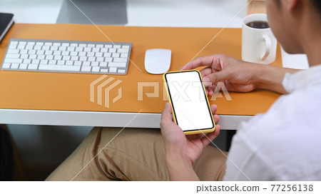 Rear view of casual man sitting at office desk and using smart phone. 77256138