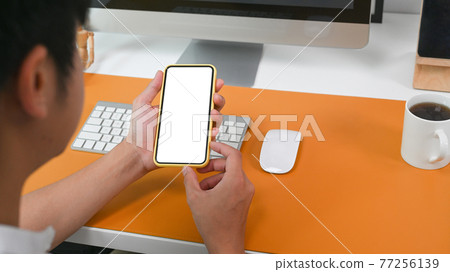 View over shoulder of businessman sitting at office desk and using mobile phone. 77256139