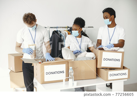 Volunteers in protective masks and gloves pack boxes 77256605