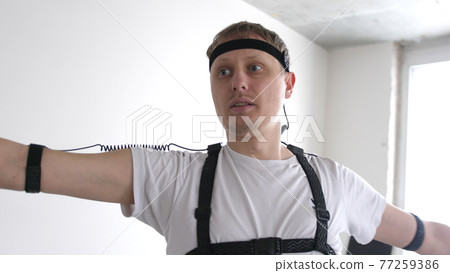 athletic man with beard wears motion capture suit with sensors headset moving in virtual reality taking something and looking at his hands excited experience cyber space online 77259386