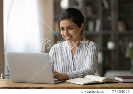 Smiling Indian woman using laptop, studying online at home Smiling Indian woman using laptop, studying online at home 77263035