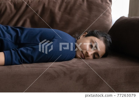 Close up exhausted Indian woman falling asleep, lying on couch Close up exhausted Indian woman falling asleep, lying on couch 77263079