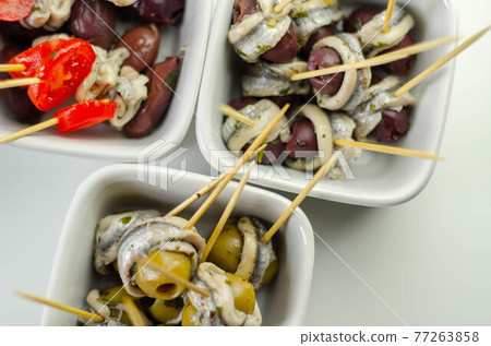 The traditional Spanish appetizers of olives, tomatoes and anchovies in a white ceramic bowls The traditional Spanish appetizers of olives, tomatoes and anchovies in a white ceramic bowls 77263858