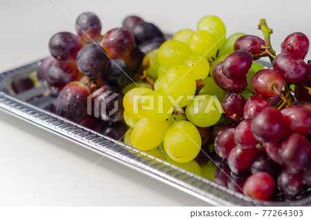 Three types of green, red and black grapes on a silver tray Three types of green, red and black grapes on a silver tray 77264303