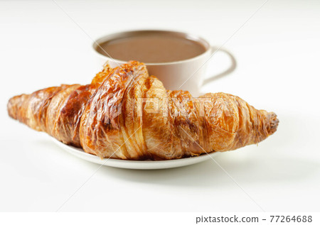 Delicious croissant on a ceramic saucer with coffee in a cup Delicious croissant on a ceramic saucer with coffee in a cup 77264688