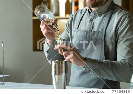 Close-up professional bartender pours rum into a shaker, making a classic cocktail in a modern trendy bar. 77264819