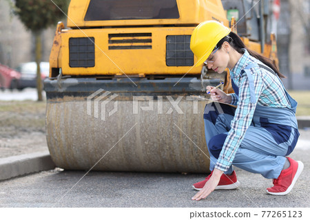 Woman examines asphalt pavement in front of asphalt paver Woman examines asphalt pavement in front of asphalt paver 77265123