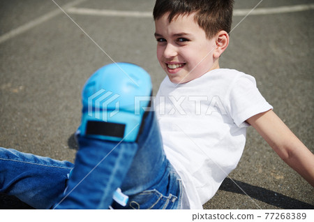Close-up portrait of a beautiful child in protective knee pads sitting on the asphalt of a sports ground on the street 77268389