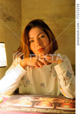 beautiful young brunette woman in a white sweater sitting at a table near a lamp with a ceiling beautiful young brunette woman in a white sweater sitting at a table near a lamp with a ceiling 77271258