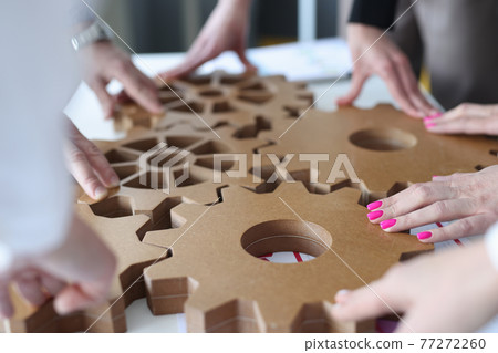Employees connect together wooden gears on work table Employees connect together wooden gears on work table 77272260
