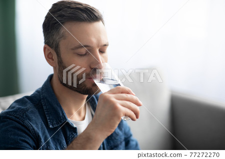 Closeup of bearded man drinking water at home 77272270