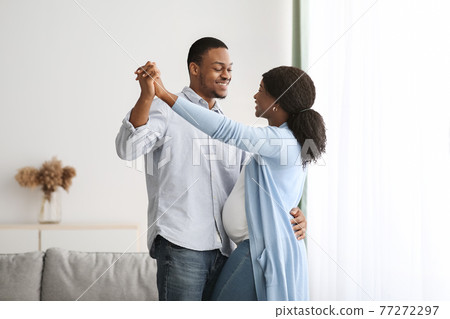 Romantic black pregnant couple dancing at home 77272297