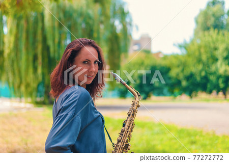 red-headed young girl in a blue jacket with a saxophone smiling in the park red-headed young girl in a blue jacket with a saxophone smiling in the park 77272772