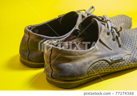 Old torn yellow summer shoes on a yellow background Old torn yellow summer shoes on a yellow background 77274388
