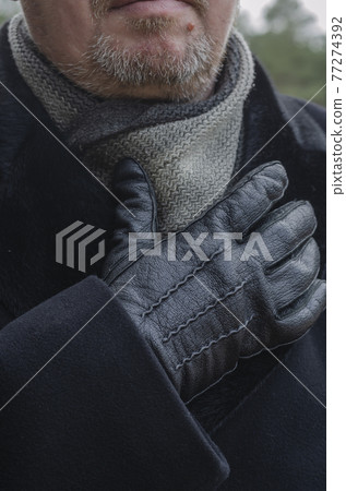 A cropped photo of a middle-aged man wearing a black coat and gloves. 77274392