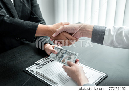 Business people shaking hands with money in hands from their partner to give success the deal contract in a corruption scam, illegal and dishonest Business people shaking hands with money in hands from their partner to give success the deal contract in a corruption scam, illegal and dishonest 77274462