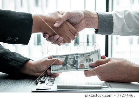 Business people shaking hands with money in hands from their partner to give success the deal contract in a corruption scam, illegal and dishonest Business people shaking hands with money in hands from their partner to give success the deal contract in a corruption scam, illegal and dishonest 77274463