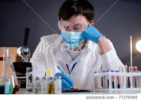 Tired, exhausted, devastated doctor scientist, after long shift, head in hands on face mask with text coronavirus. Lost hope concept, Covid-19 disease, global pandemic outbreak, SARS-CoV-2 Tired, exhausted, devastated doctor scientist, after long shift, head in hands on face mask with text coronavirus. Lost hope concept, Covid-19 disease, global pandemic outbreak, SARS-CoV-2 77276995
