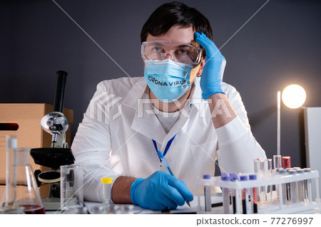 Young doctor very tired and infected with covid 19, upset holds his head with hands, raises head on his face mask with the words written on mask coronavirus. Medical system collapse during pandemic Young doctor very tired and infected with covid 19, upset holds his head with hands, raises head on his face mask with the words written on mask coronavirus. Medical system collapse during pandemic 77276997