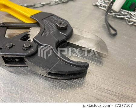 Large iron sharp metal scissors, metal cutters with chains, lie on an iron table. Hand-held locksmith tools. The background 77277107
