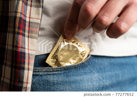 Close up of young man taking condom out of pocket in jeans. Remember about protection. Safe sex, AIDS. Pulling out condom gold color. Safety sex concept. Contraception. Contraceptive. World AIDS day 77277652