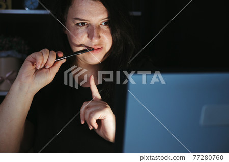 Young focused woman working at laptop at night Young focused woman working at laptop at night 77280760