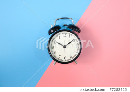Black vinatge alarm clock with pink and blue background. Black vinatge alarm clock with pink and blue background. 77282523