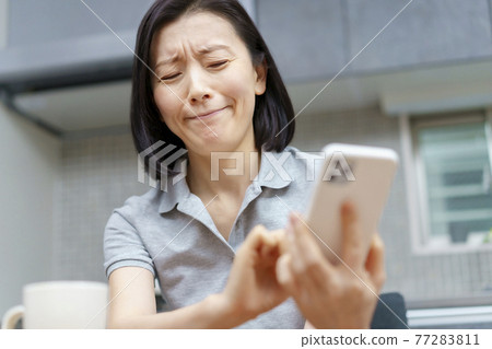 A woman looking at a smartphone with a stressed expression A woman looking at a smartphone with a stressed expression 77283811