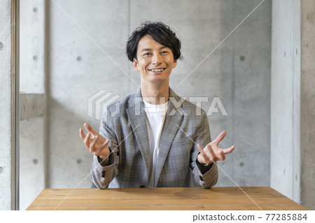 A smiling young man talking looking at the camera 77285884