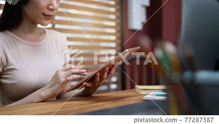 A asian female student sitting at the table, using tablet when studying online at home A asian female student sitting at the table, using tablet when studying online at home 77287387