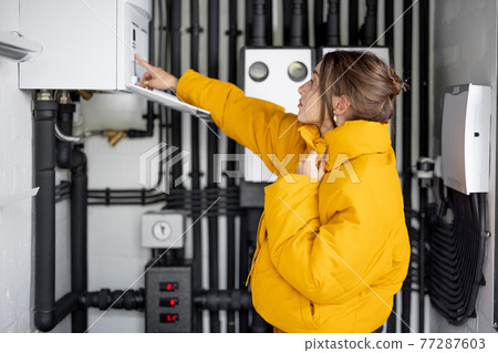 Woman adjusts heating temperature in the boiler room 77287603
