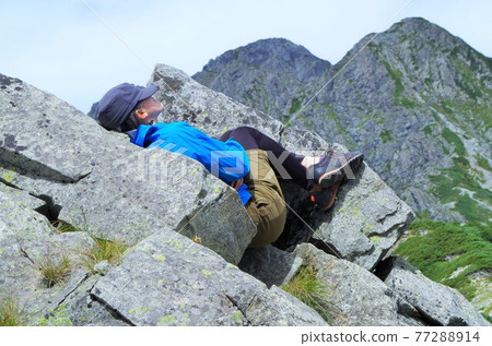A female climber takes a nap on a rocky area with Mt. Tsurugidake in the background. 77288914
