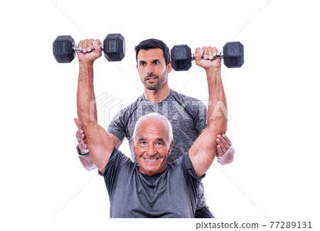 Elderly male client exercising with a fitness trainer, lifts dumbbells. On a white isolated background. 77289131