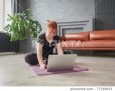 Woman sitting cross-legged on yoga mat and looking Woman sitting cross-legged on yoga mat and looking 77289853