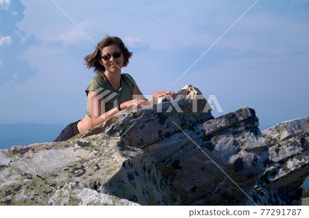 Smiling woman resting on top of cliff after climbing Smiling woman resting on top of cliff after climbing 77291787