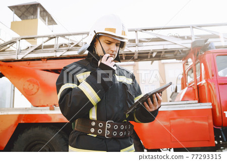 Male firefighter with tablet in uniform on car background 77293315
