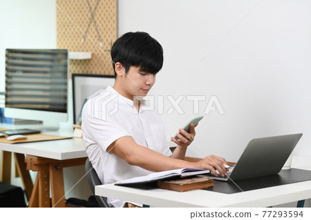 Young man employee working with laptop computer and using mobile phone in home office. Young man employee working with laptop computer and using mobile phone in home office. 77293594