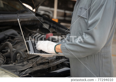 Mechanic using a laptop computer to check collect information during work a car engine. service maintenance of industrial to engine repair. 77294010