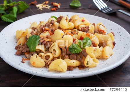Stewed pasta with minced beef and vegetables, macaroni in Navy style on a plate. Dark wooden background. Stewed pasta with minced beef and vegetables, macaroni in Navy style on a plate. Dark wooden background. 77294440